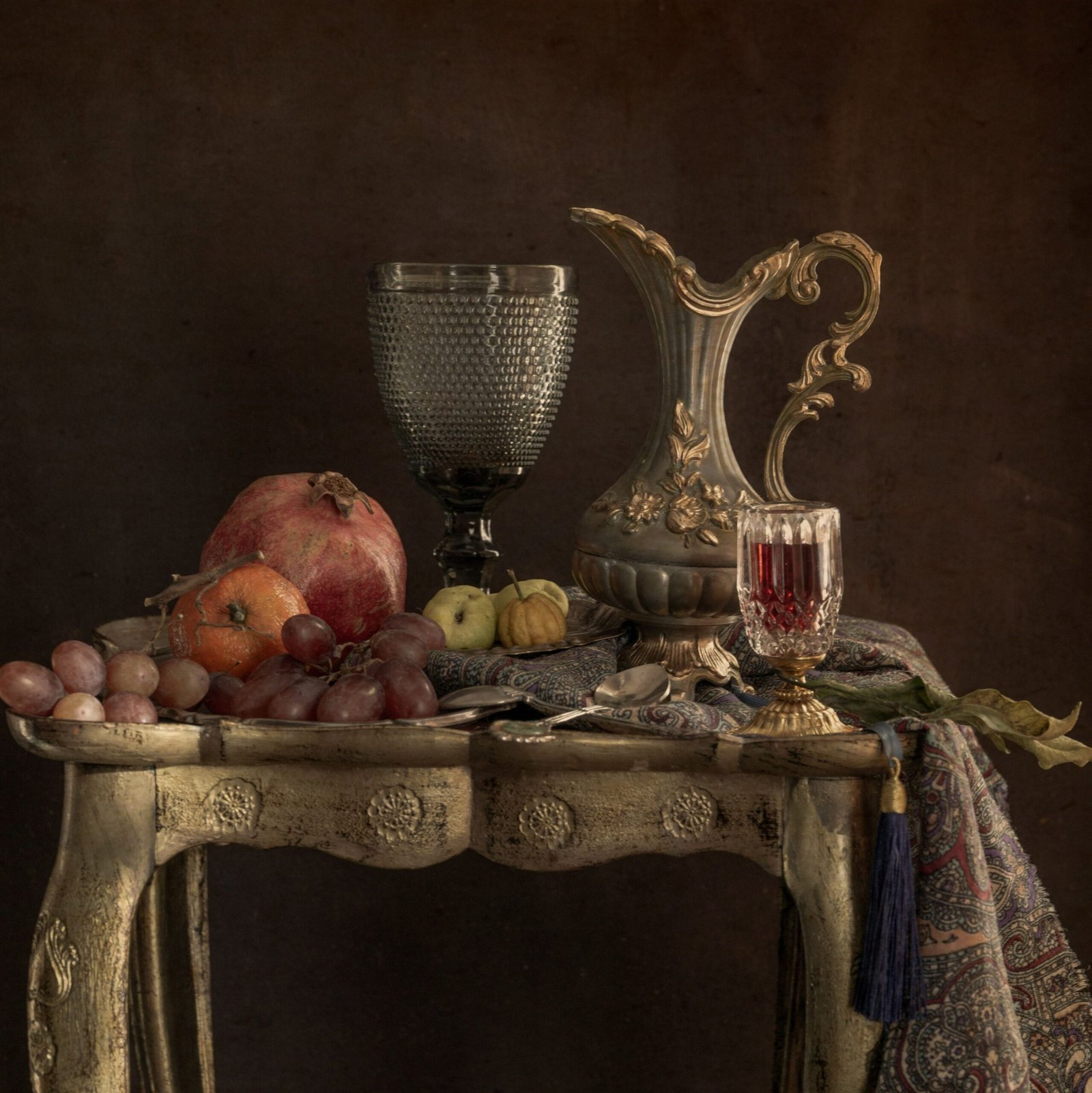 A classic still life composition featuring fruits, an ornate pitcher, and delicate glassware on a vintage table.